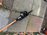 Partial view of black chainsaw head and orange pole lying on interlocking pavers