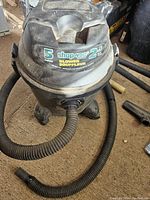 Front and top view of the 5 gallon black Shop Vac showing hose attached, brand and blower details visible.