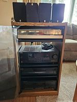 Full view of AV system components stacked in a wooden rack with glass door, including Yamaha AV receiver, Sony CD player, Scott cassette deck, and Pioneer turntable on top.