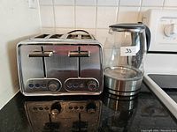 Side view of stainless steel Hamilton Beach 4-slice toaster and Megawise glass electric kettle on black countertop.