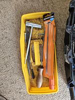 Yellow plastic tray containing chain saw sharpening files in orange packaging, wooden-handled file, chisels, and other hand tools.