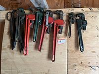 Wide photo showing 3 vice grips on left side, 7 pipe wrenches with red and green handles arranged in the middle, and 2 tin snips black metal cutters on the far left.