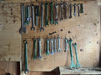 Overall view of metric and standard combination and adjustable wrenches on wooden board with sizes marked.