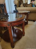 Side view of the two matching round end tables, showing wood legs, lower shelf, and glass tops.