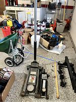 Two hydraulic floor jacks placed on a garage floor; Pittsburgh heavy duty 3 ton floor jack is larger, alongside a smaller hydraulic floor jack with handle.