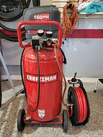 Front view of red Craftsman air compressor on wheels with attached black and red hose reel.