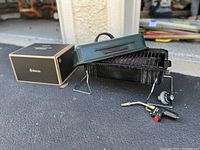 Green metal Sunbeam cook stove opened with grill surface, fold-out legs, and connected propane burner.