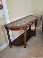 Front side view of console table showing wood frame, glass top with metal scrollwork, four legs, and bottom shelf.