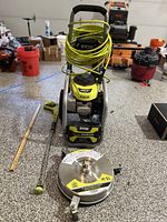 Full view of Ryobi pressure washer with coiled high-pressure hose, spray wand, and surface cleaner attachment