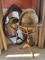 Globe positioned in front of ornate oval mirror showing both items together