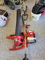 Full view of Toro blower vac red with black nozzle and handle, Echo trimmer laying side by side on floor