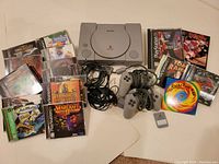 Full lot arranged on white background showing console, controllers, memory card, cables, multiple game cases and loose disc