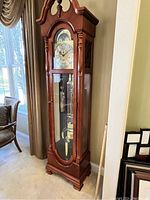 Full view of clock showing cherry wood case, arched glass door and visible weights and pendulum