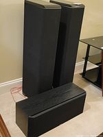 Two tall Boston Acoustics VR950 floor-standing speakers and one Boston Acoustics VR12 center channel speaker with black speaker grilles, all placed on carpet.