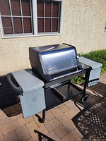 Full view of Weber gas grill with closed stainless steel hood, two side shelves, and cart base with wheels in outdoor setting