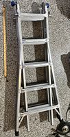 Collapsed ladder showing aluminum rungs and locking sections next to measuring stick