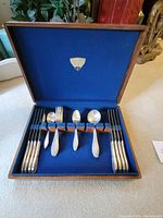 Flatware set arranged inside the wooden case showing six dinner knives, six dinner forks, two teaspoons, and two tablespoons with blue velvet interior