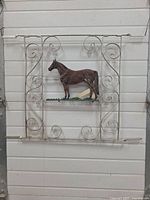 Full view of the white painted riveted frame with decorative scrollwork surrounding the 3D cast aluminum horse mounted in the center.