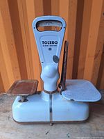 Side view of Toledo meat scale showing porcelain base and metal weighing trays, with visible rust and wear.