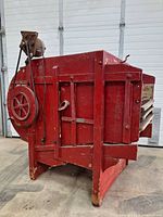 Side view of antique red wooden seed shaker with electric motor and belt pulley system attached.