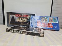 Photo showing all three game boxes: 1995 Star Wars Monopoly, 1975 Six Million Dollar Man, and 1977 Star Wars board game
