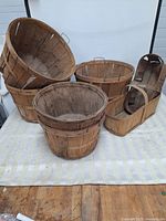 Front view of six wooden bushel baskets and trugs arranged on cloth, showing varied shapes and wood patina.