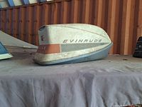 Front-right angled view of vintage Evinrude Ski-Twin outboard motor cowling on fabric surface with rust-colored corrugated metal background.