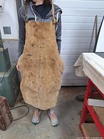 Front view of the heavy leather apron worn by a person, showing the full length from neck to below the knees, visible signs of wear and dirt marks.