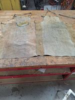 Two stained leather aprons side by side on a wooden workbench.