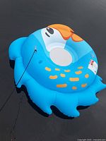 Overhead view of the large blue and orange bird-shaped inflatable swim tube floating on water with a black rope attached.