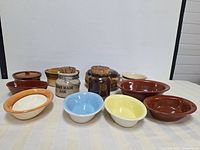 Multiple brown, beige, yellow, blue ceramic bowls and lidded jars arranged on a surface