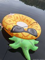 Swim tube floating on water, designed as a pineapple with sunglasses and green leaves base, showing its size and features.