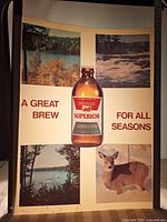 Full view of the lighted advertising insert showing central beer bottle and four outdoor scenes with text.