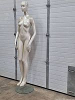 Side view of vintage fiberglass female mannequin standing on a round glass base.