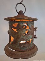 Front view of rusted cast iron lantern showing hummingbird cutout design with tea light lit inside.