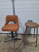Two vintage stools side by side on concrete floor; one upholstered swivel with metal base, one rustic wooden seat with metal base.