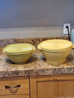 Photo of two round yellow vintage Tupperware bowls with matching lids on countertop, showing size difference and lid design.
