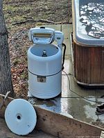 Full view of the Viscount VR100 washing machine outside next to a hot tub, showing the tub, lid removed, and wringer mechanism.
