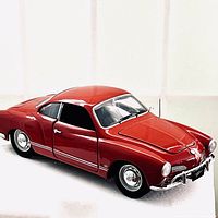 Front angled view of red 1967 Volkswagen Karmann Ghia diecast model showing chrome bumper, wheels, and door open.