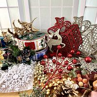 Wide view showing four spools of decorative Christmas ribbon, assorted pine cones, red berry spray picks, and crocheted white snowflake and butterfly shapes.