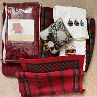 Overview of all Christmas themed linens including folded blankets, plaid tablecloth, small wreath pillow, and kitchen towels