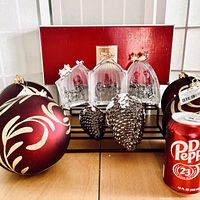 Lot showing three-piece Mikasa frosted glass nativity set with gold stars, two silver pinecone ornaments, four oversized red and gold Christmas ball ornaments, Dr Pepper can for scale