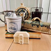 Overview of all items including the Wisconsin Homestead crock, small brown crock, pottery covered butter dish, carved building model, and Native pottery jug.