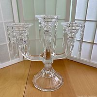 Front view of the three-branch crystal candelabra showing the central column, arms, and hanging crystal prisms.