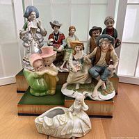 Group photo of vintage figurines showing a variety of porcelain and bisque collectible figures including peasant couples, Victorian styled woman, old man and woman, and planters.