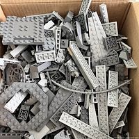 Top-down view of box with various gray LEGO bricks including plates, wing pieces, and standard bricks in light and dark gray shades.