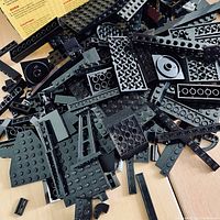 Top view of assorted black LEGO bricks and pieces showing flat plates, angled and circular pieces scattered in a box.