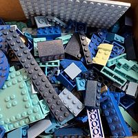 Close-up photo showing assorted blue LEGO pieces including flat plates and bricks in shades from dark blue to pale blue.