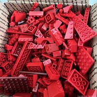 Open box filled with various red LEGO bricks and pieces in different shapes and sizes.