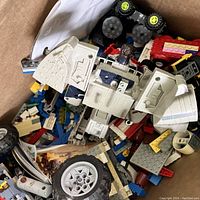 Box with a partially built white and blue LEGO robot or mech, visible black wheels, and various colorful LEGO bricks and pieces inside.